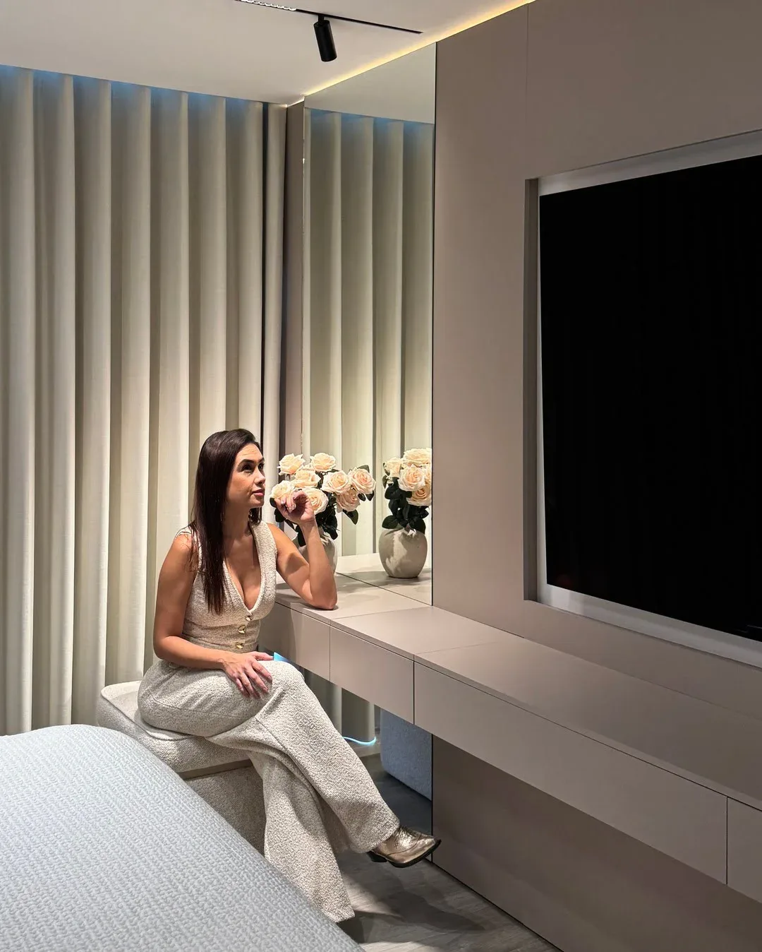 Mujer sentada frente a un mueble vanity con espejo grande y pantalla de televisión.