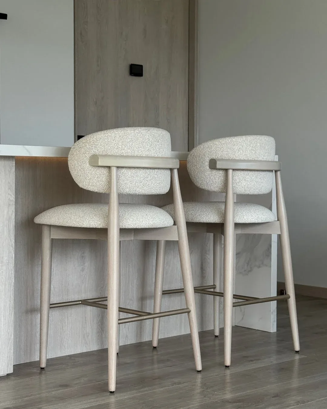 Vista trasera de un taburete alto de cocina tapizado con patas de madera clara.