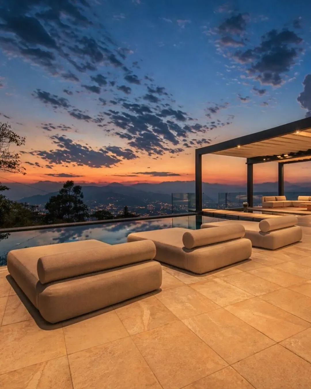 Terraza al atardecer con mobiliario acolchado, vistas panorámicas y ambiente sereno.