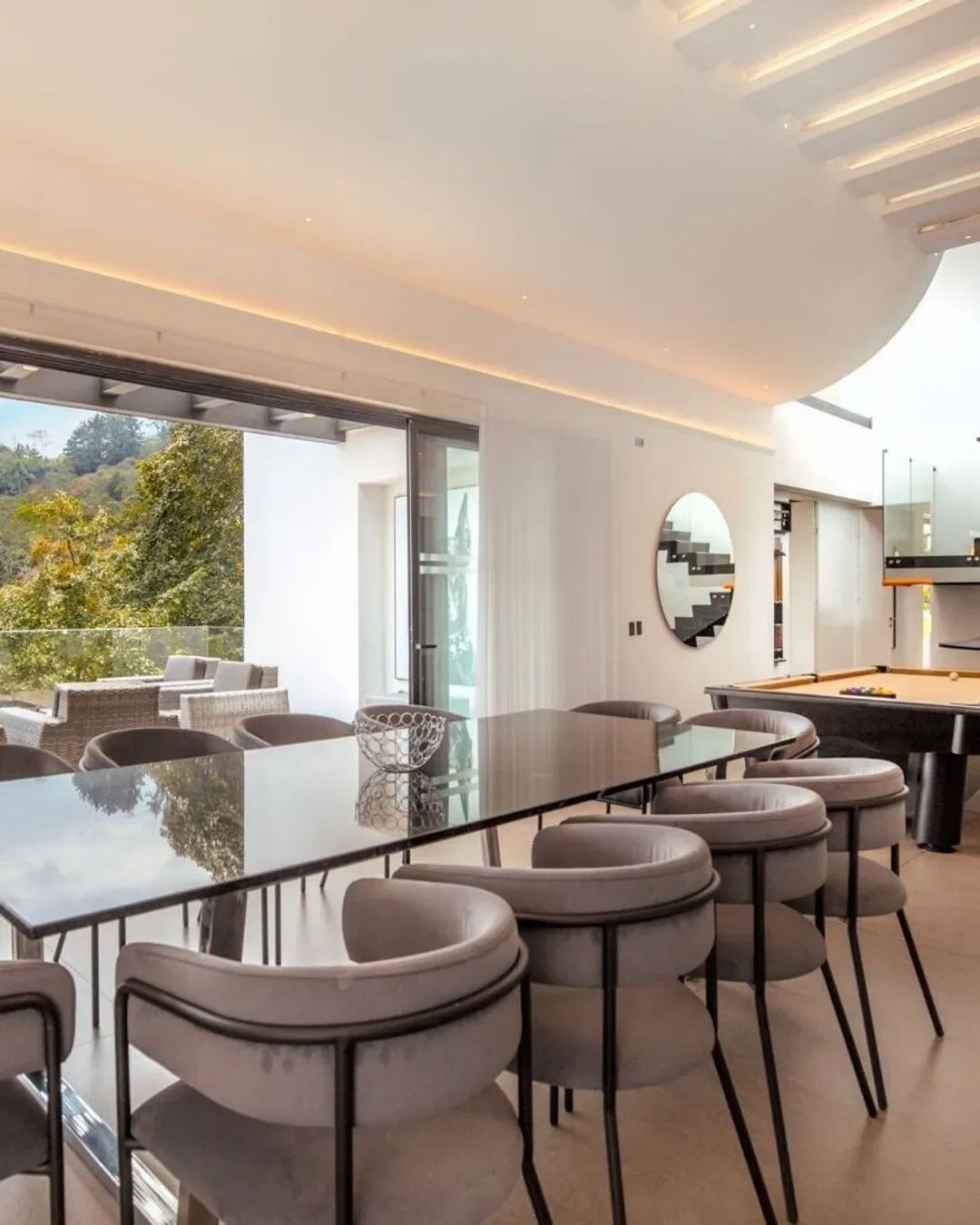 Comedor contemporáneo con sillas envolventes y conexión visual con la naturaleza.