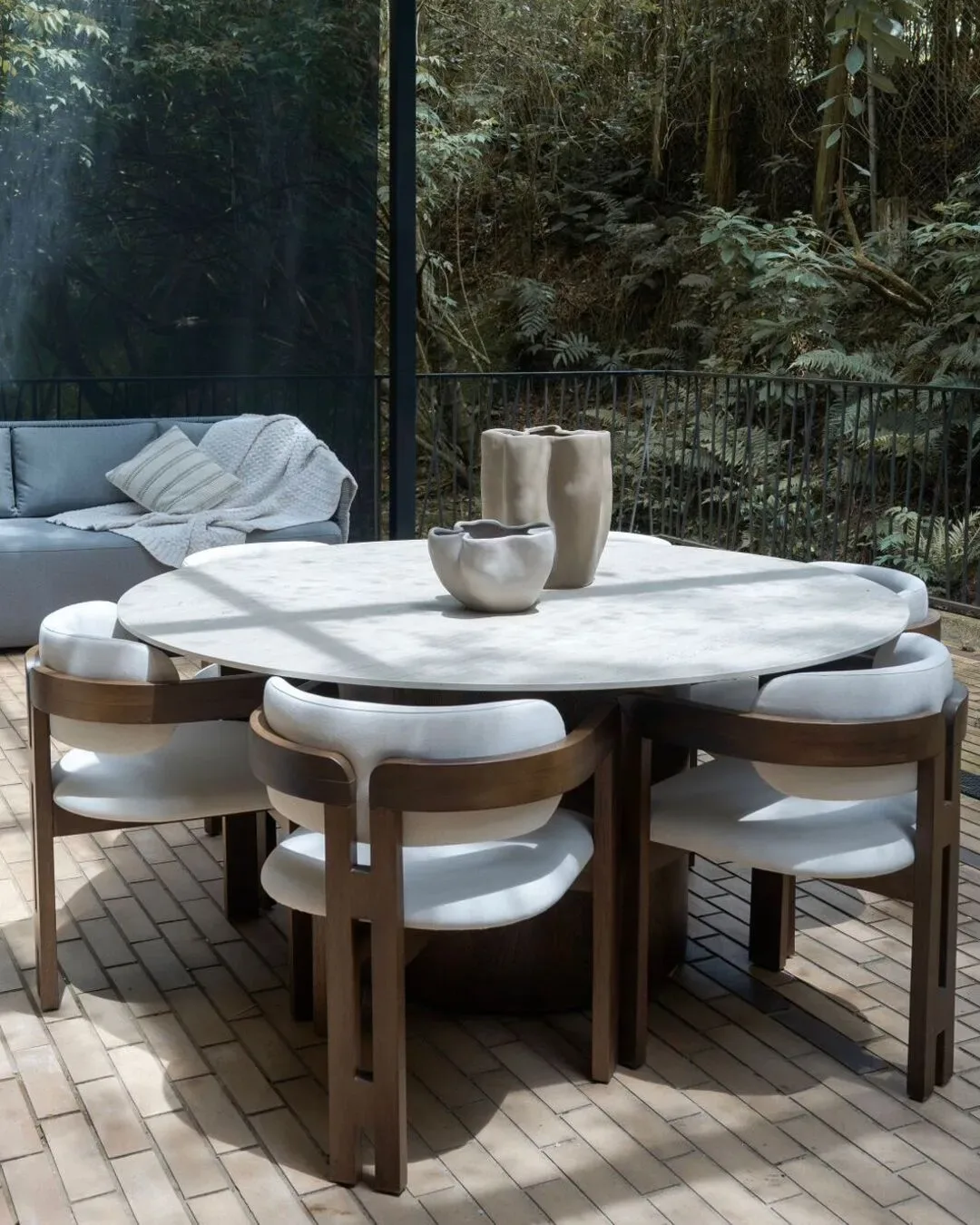 Mesa circular de madera con sillas de estructura oscura y espaldar curvo tapizado en blanco.