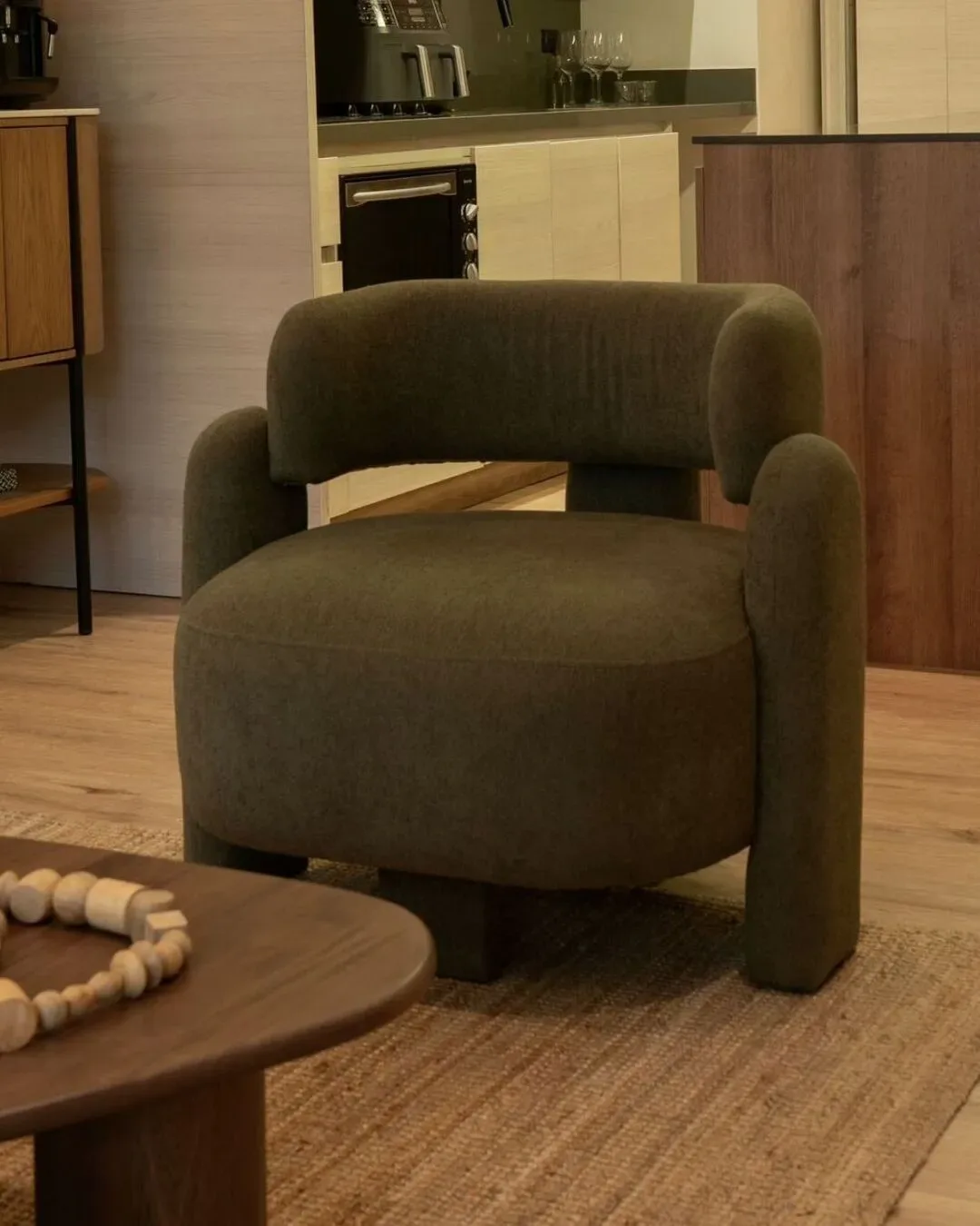Poltrona ergonómica tapizada en textil verde oliva con base de patas cilíndricas de madera.