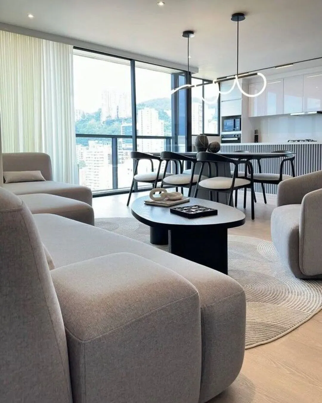Sala sofisticada con sofá modular, comedor negro, luz natural y vista urbana de Medellín.