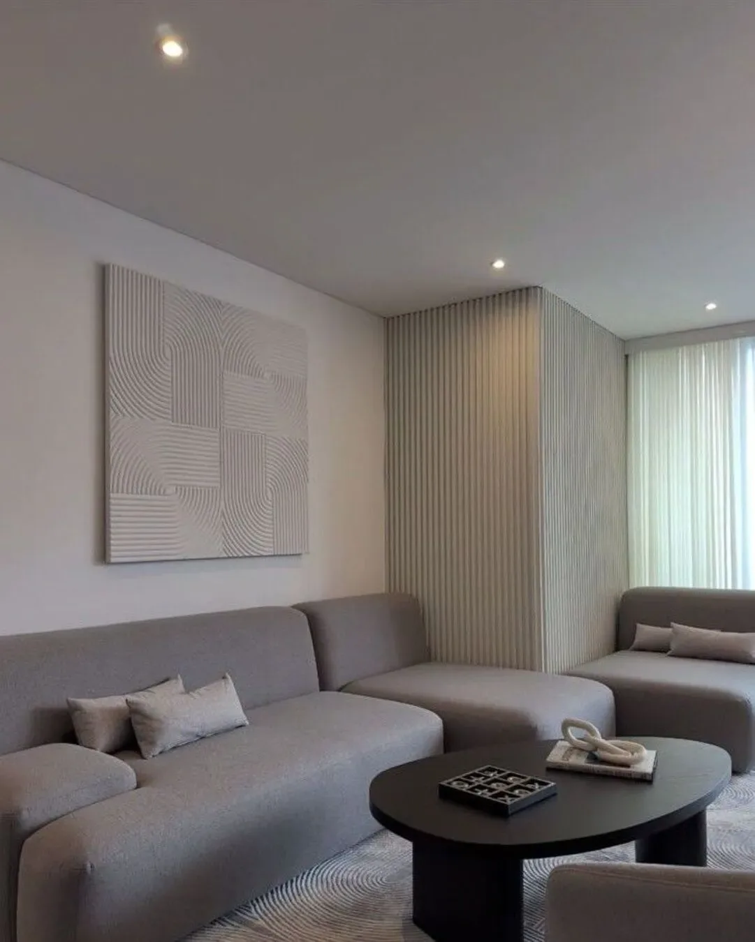 Sala elegante con tonos neutros, texturas geométricas, sofá modular y mesa central negra.