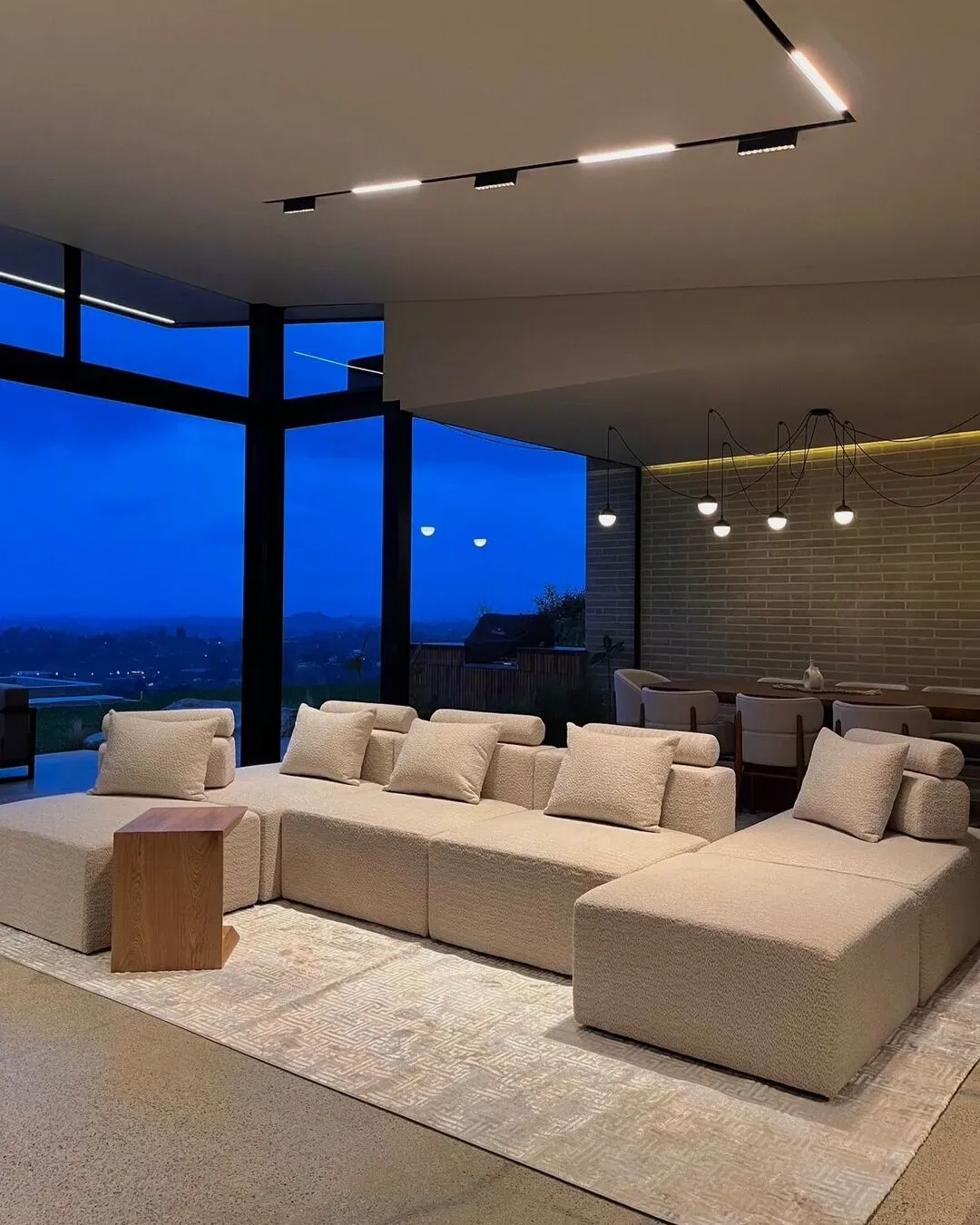 Sala amplia con sofá modular de alto confort, iluminación cálida y vista abierta al paisaje.