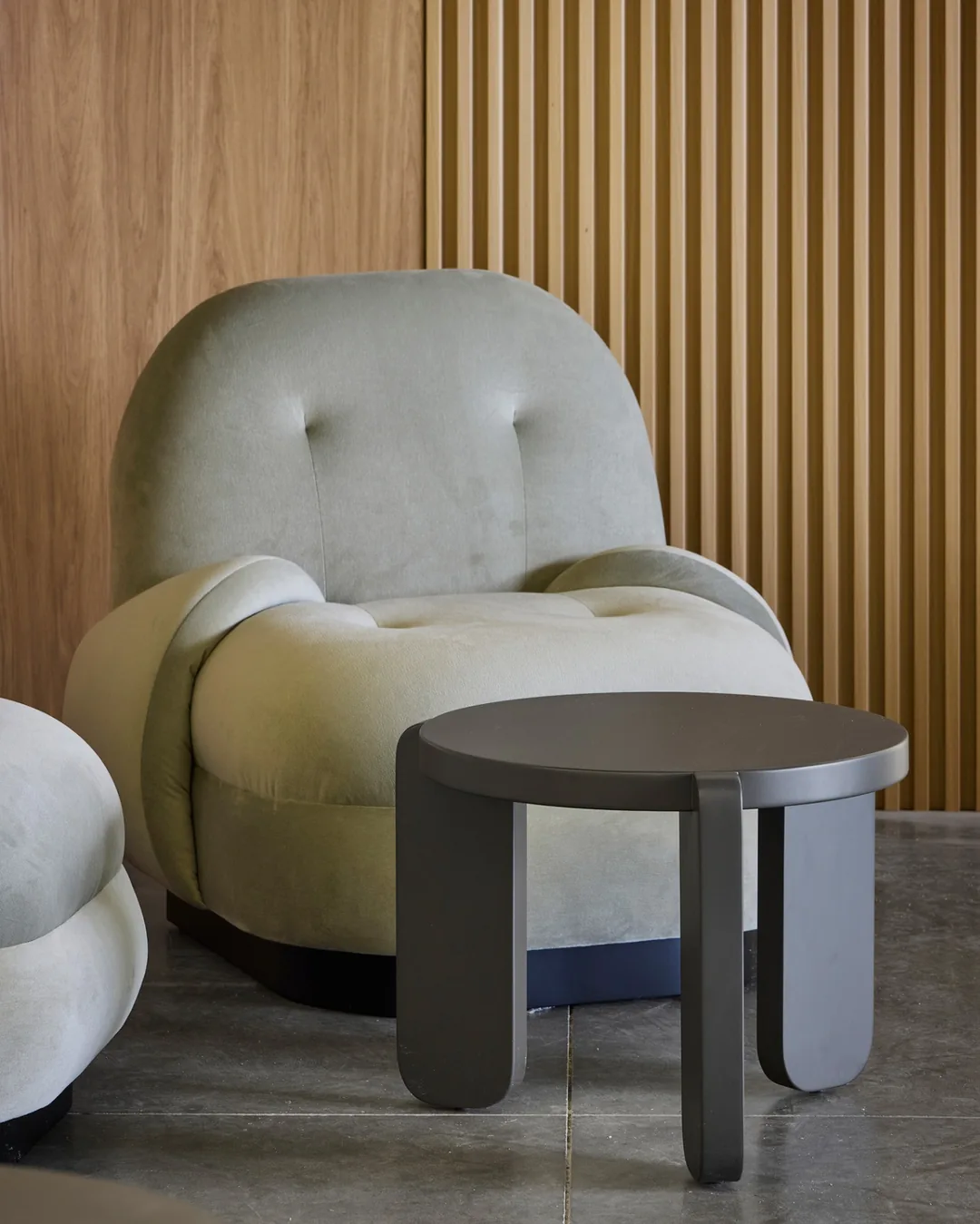 Sillones tapizados en verde con mesa auxiliar circular negra frente a panel en madera de diseño cont