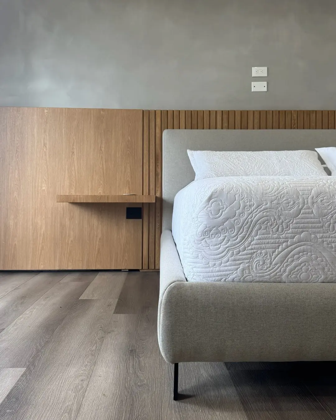 Primer plano de una cama con detalles de madera acanalada en la pared y textiles blancos.