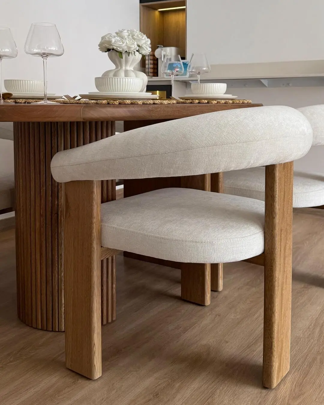 Detalle de una silla de comedor tapizada en tela clara con estructura de madera, junto a una mesa de