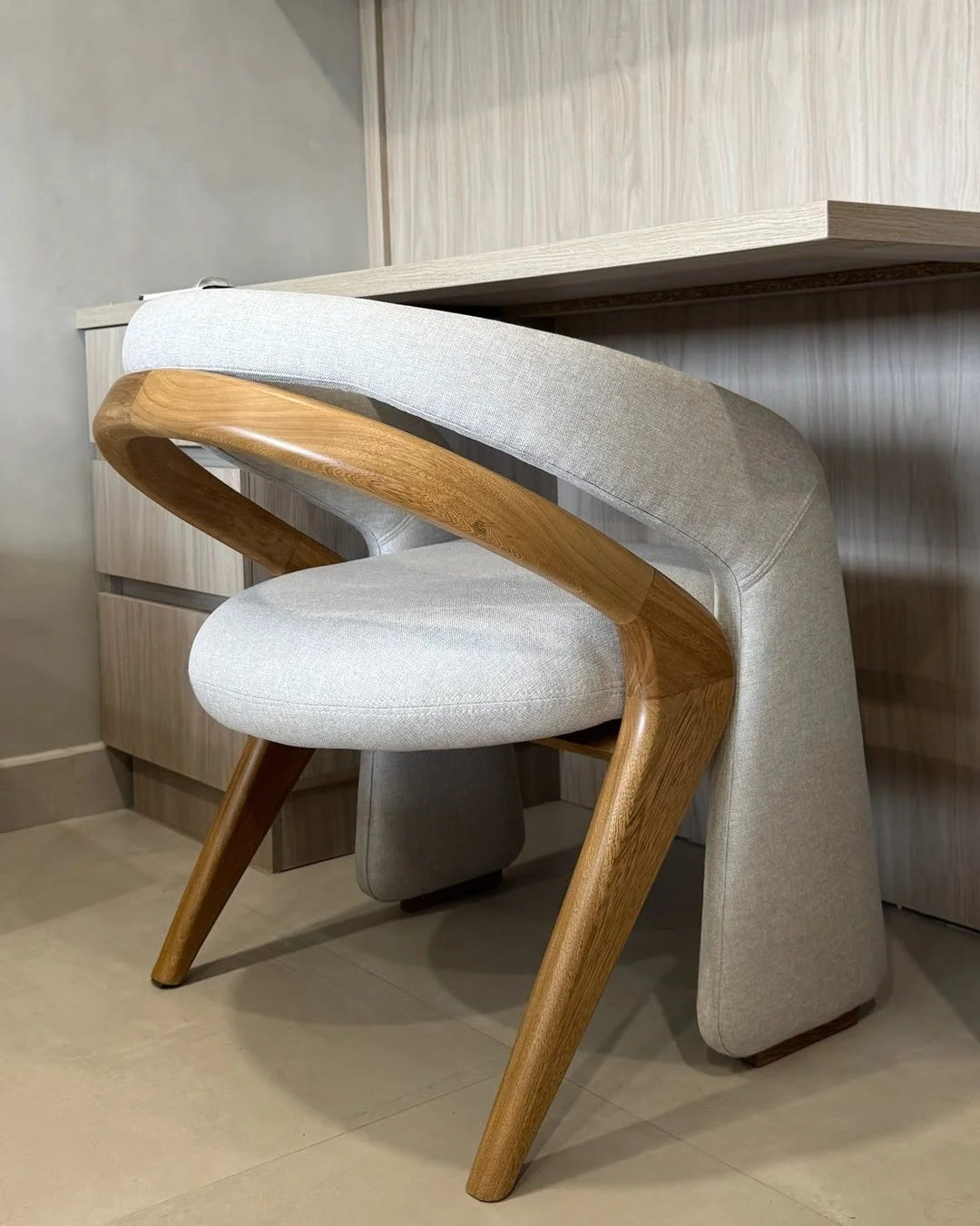 Silla de escritorio con estructura de madera curva y tapizado en tela clara, diseño ergonómico.